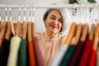 Stylish senior woman with silver hair smiles while browsing through colorful clothing racks in a modern boutique setting