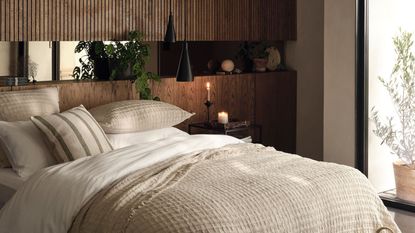 A warm rustic bedroom with wooden headboard stretching along a whole wall, and a large bed with neutral bedding