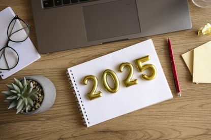 The numbers 2025 sitting on a notebook on a desk with pencil, plant and glasses