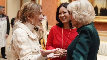 Geri Horner wearing an ivory jacket talking to Queen Camilla as a woman in a red dress looks on 