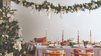 A dining room with a set table for a Christmas dinner with a white bow-decorated Christmas tree set next to the table