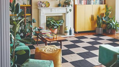 A living room with a green sofa, yellow cabinets, a black and white chequered rug and cube-shaped ottomans