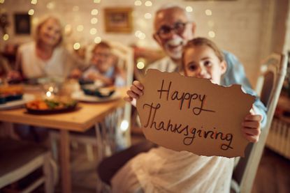 Close-up of girl holding Thanksgiving sign while having family dinner at home