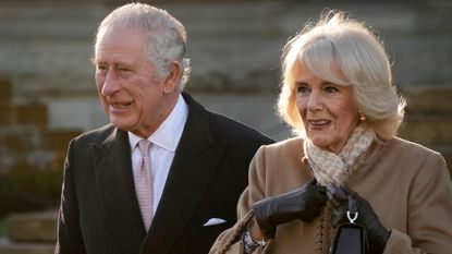 Queen Camilla and King Charles wearing coats standing next to each other outside and smiling