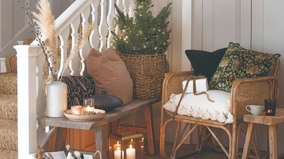 A hallway with a staircase decorated for Christmas with a small tree on top of a seating bench and lit candles