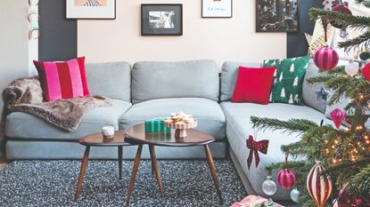 A living room with a grey corner sofa decorated for Christmas with festive cushions and a Christmas tree