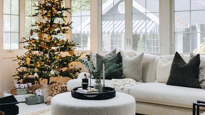 christmas living room with white sofa and green pillows, christmas tree, and round ottoman coffee table