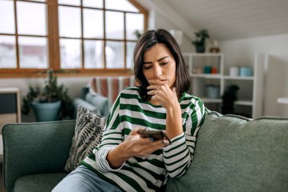 Concerned young woman using smart phone in a living room