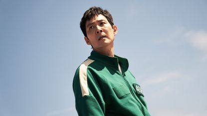 Lee Jung-Jae as Gi-hun, wearing the green tracksuit and standing with the sky behind him, in &#039;Squid Game.&#039;