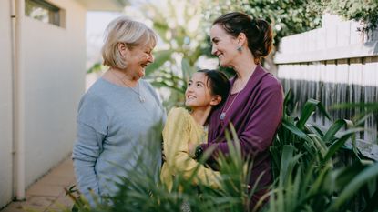 A grandmother, granddaughter and daughter smile while standing outside.