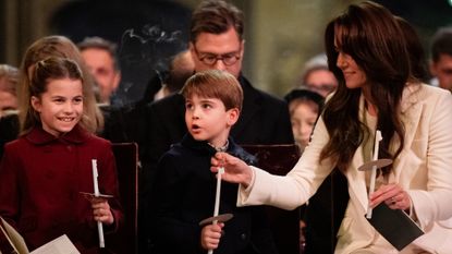 Princess Charlotte and Prince Louis holding candles at a carol service while Princess Kate adjusts Louis&#039;s candle