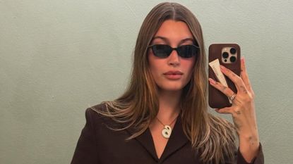 Hailey Bieber wears a brown skirt suit with sunglasses and a B initial necklace