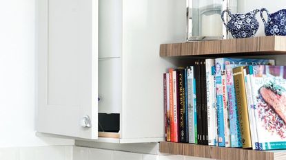 A hot water boiler stored in a tall wall kitchen cupboard unit, with shelves and wood worktop