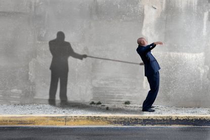 A man&#039;s shadow pulls him backward with a rope as a metaphor for fees holding you back.