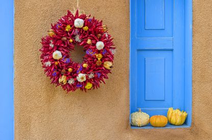 red chile wreath on building with gourds on a blue ledge