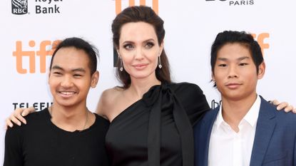 Angelina Jolie poses with two of her sons, Pax and Maddox, while wearing a one-shoulder black dress