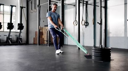 Man in gym walking backward holding straps attached to sled with four weight plates on it