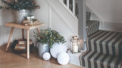 A hallway with a staircase covered in a striped runner with paper Christmas decorations, presents and lanterns on the floor