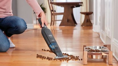 Black+Decker 12V MAX Dustbuster handheld vacuum cleaning dog food on wooden floor