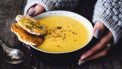 3/4 shot of a bowl of yellow soup with hands gently holding the bowl 