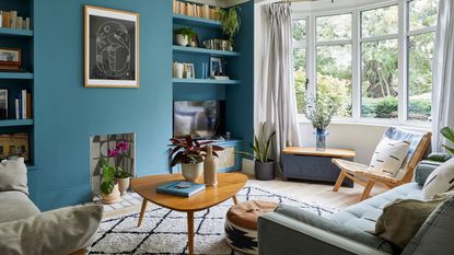 A small living room with a blue-painted feature wall with alcoves, a berber-style rug on the floor and light blue sofa