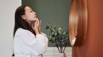 woman with glowing skin applying korean skincare to her face in the bathroom