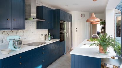 kitchen with blue cabinets, white counters, chevron ashy hardwood floors with a potted fern on kitchen island