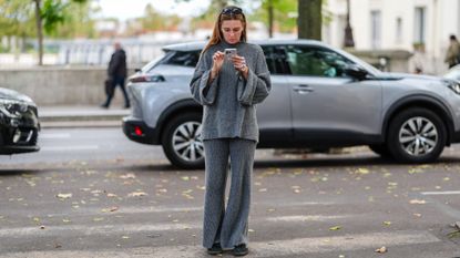 A guest wears black sunglasses, a grey wool turtleneck pullover, matchings pants, dark green sneakers shoes, during Womenswear Spring/Summer 2025 as part of Paris Fashion Week on September 30, 2024 in Paris, France. (