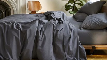 Side view of gray sheets and pillows on a bed against a white wall. 