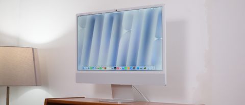 Apple iMac on a wooden desk against a white wall next to a lamp