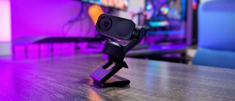 The Insta360 Link 2 webcam on a desk with violet backlighting, attached to its magnetic stand and extended.