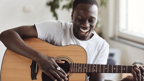 Man smiling while playing acoustic guitar