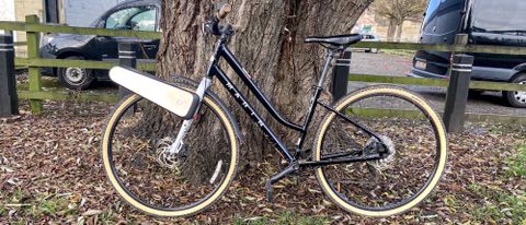 a black city bike is photographed with the CLIP e-bike conversion kit attached to the front wheel