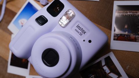 The Fujifilm Instax Mini SE sits on a table with instant film pictures