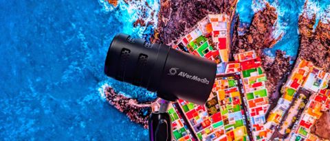 The AVerMedia VERSATI go (AM310G2) microphone held in front of a background depicting a vibrant coastal city from above.