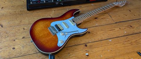 A Harley Benton ST-Modern Plus lying on a wooden floor next to a pedalboard