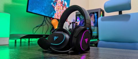 Two Razer Barracuda X Chroma headsets leaning against each other on a desk with a green backlight.