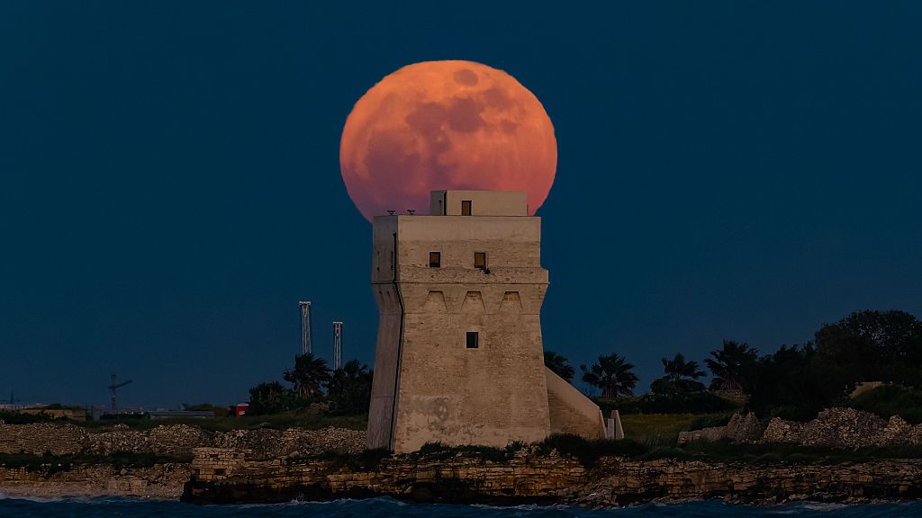 Uma vibrante lua cheia laranja atrás de uma grande torre de pedra.