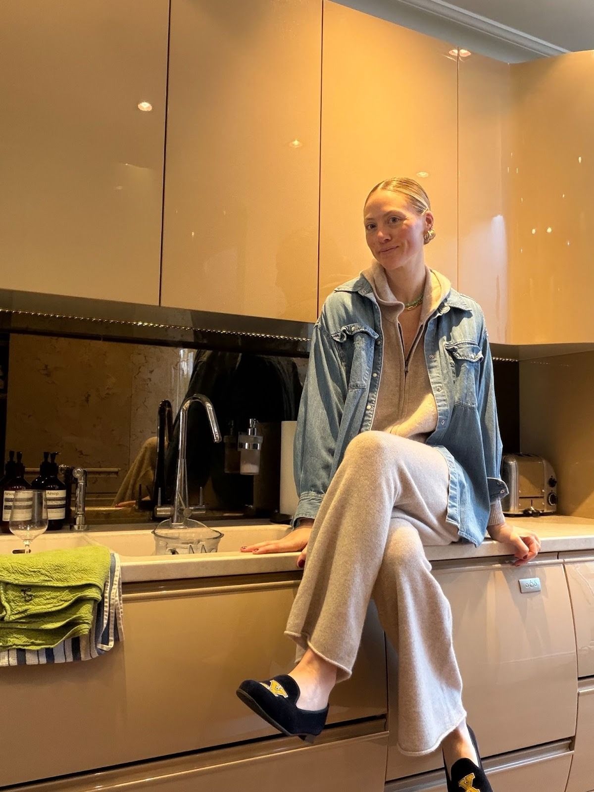 Brooke Ely Danielson sitting on a kitchen countertop wearing a denim jacket, a sweat set, and black loafers