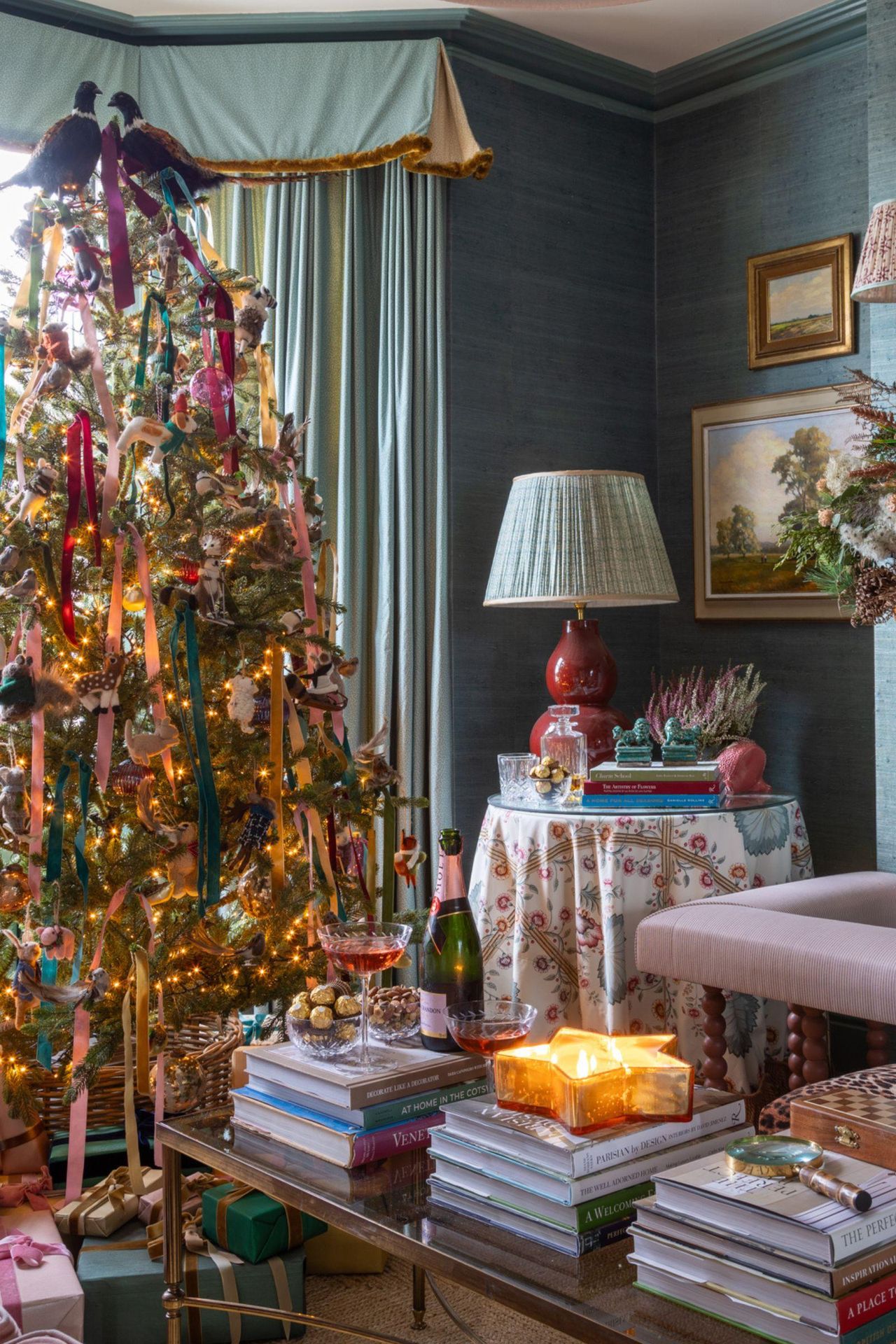 traditional english country living room wallpapered in blue grasscloth styled for christmas with a large velvet ribbon adorned tree topped with two faux pheasants and a fireplace styled with a large garland and dried oranges