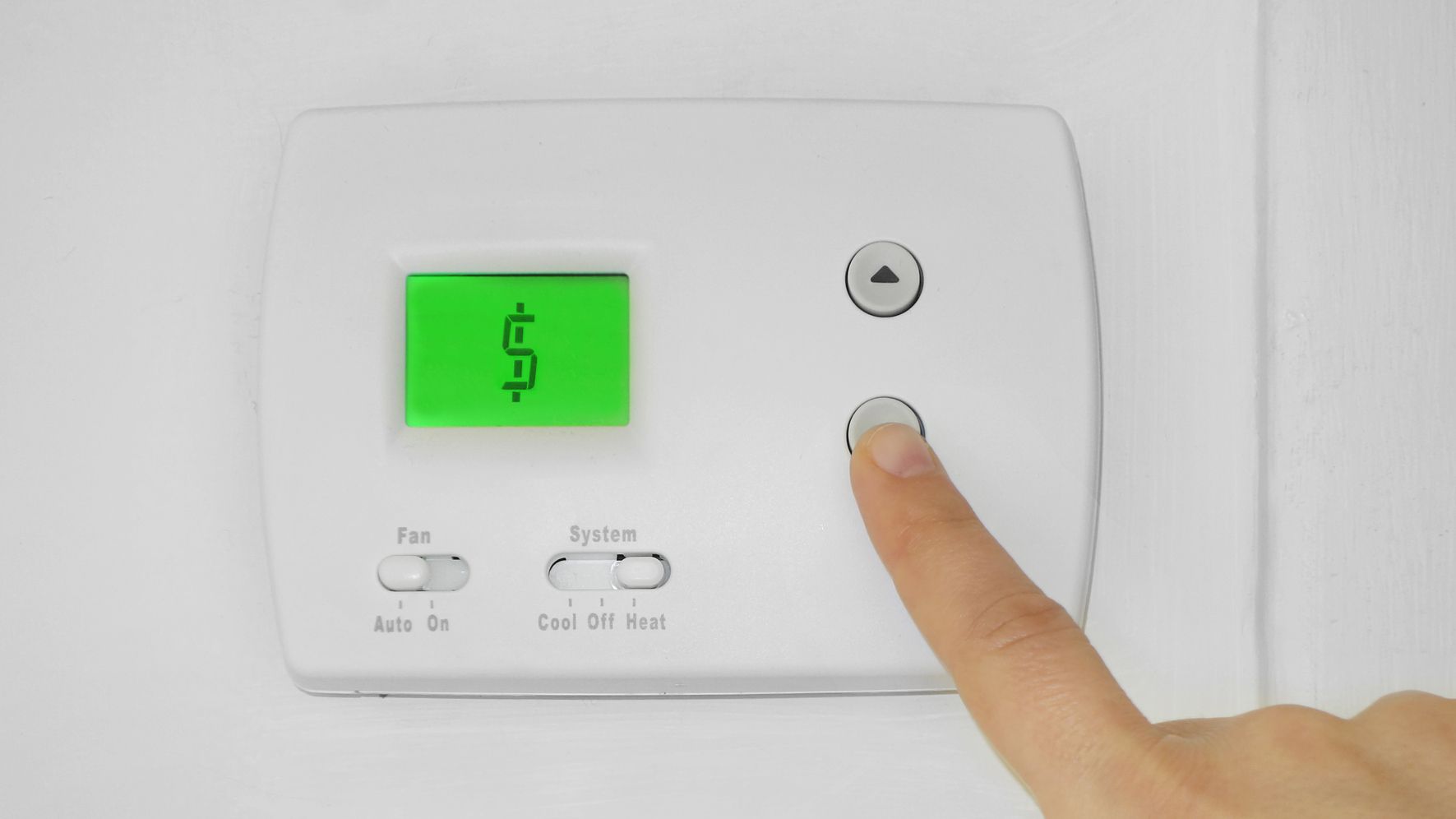 Finger pressing a button on a thermostat that displays a dollar sign, indicating rising energy costs.