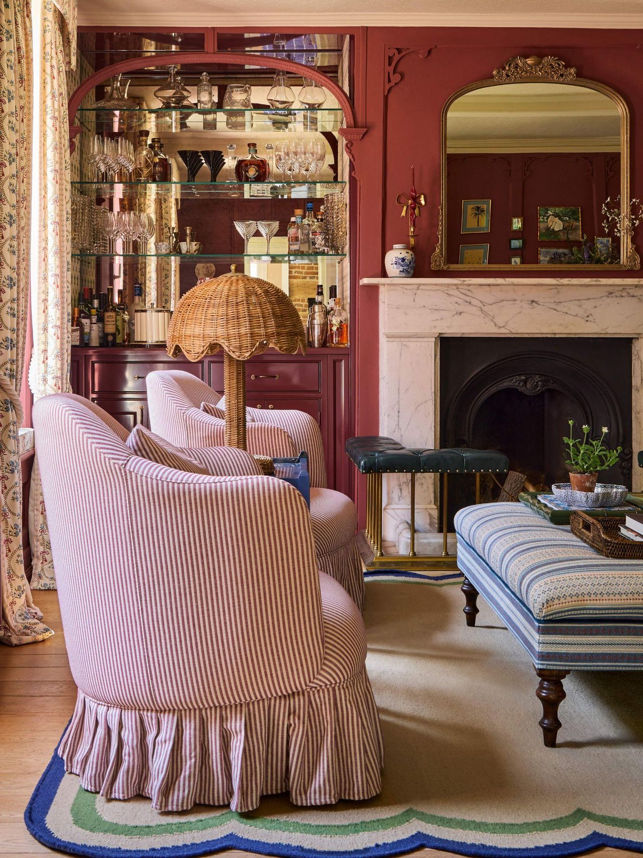 a reddy pink painted drawing room with ornate moldings, a custom mirror arched home bar and a marble fireplace