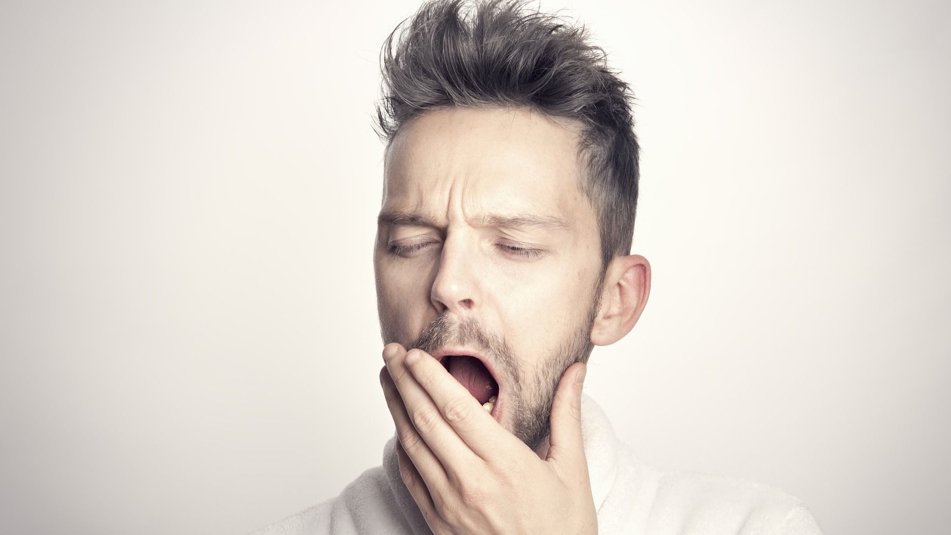 A man with gray hair holds his hand over his mouth as he yawns