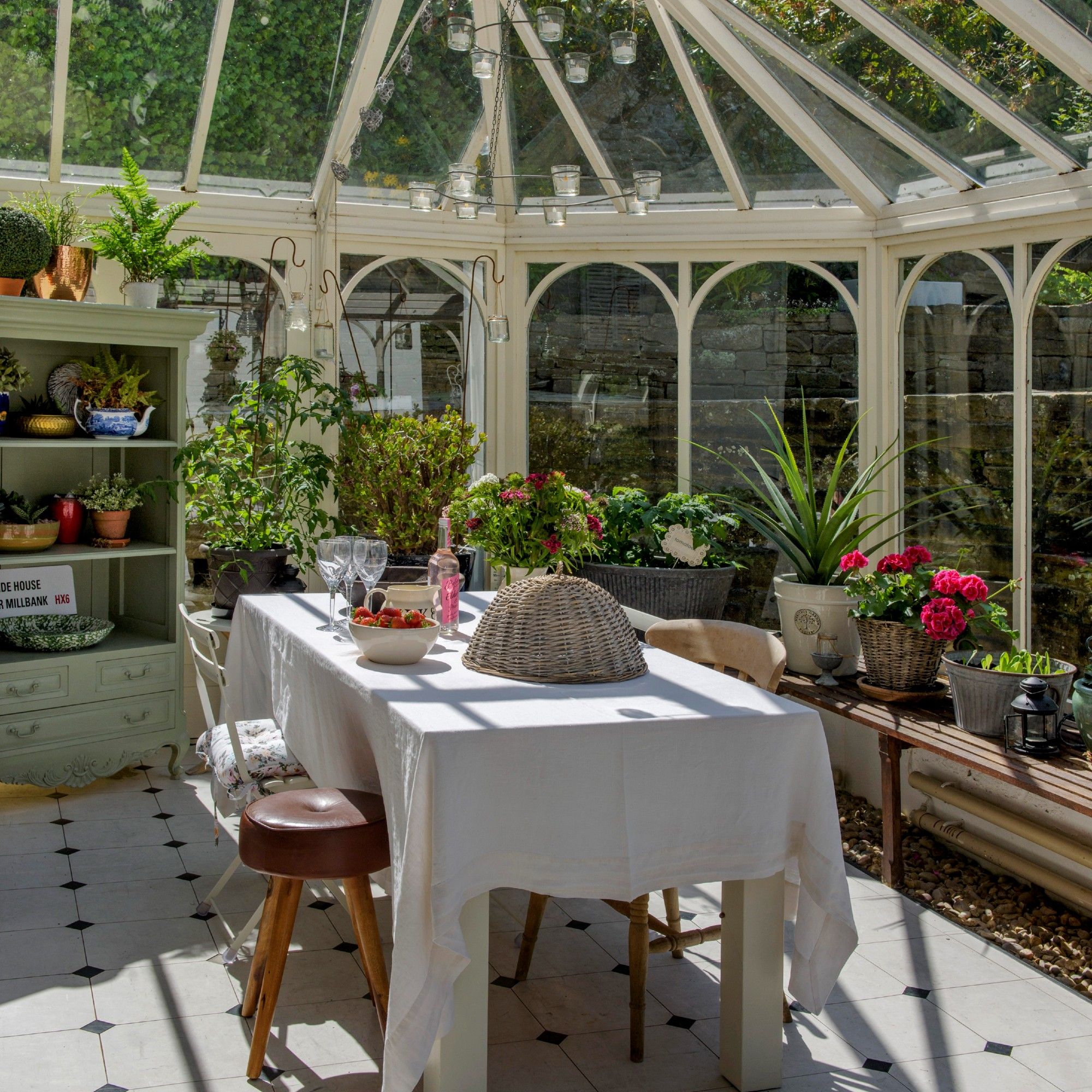 A conservatory with a dining table and mis-matched chairs in the middle and a sage green display cabinet to the side