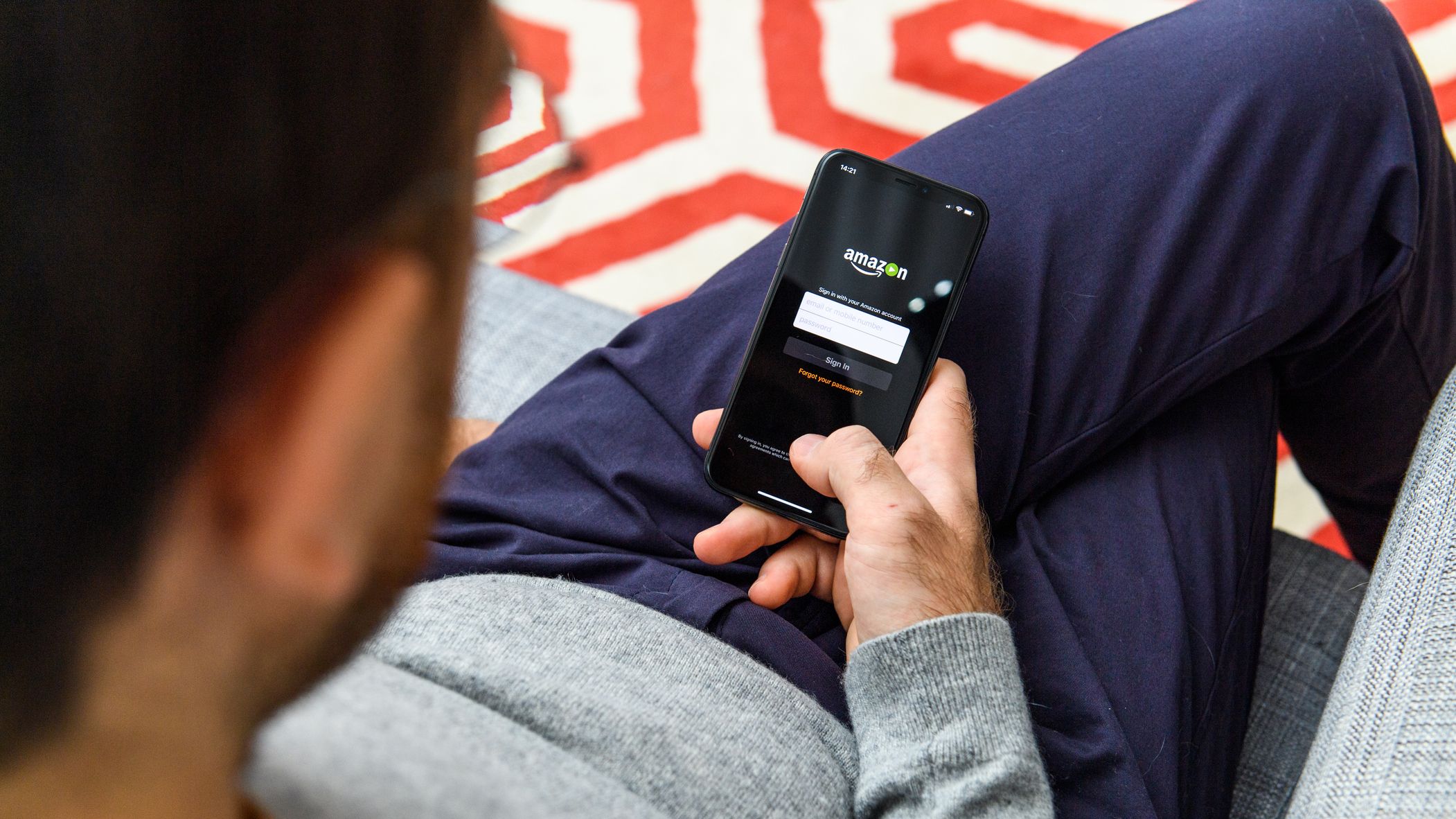 Man logging into Amazon on his mobile phone while sitting on a couch.