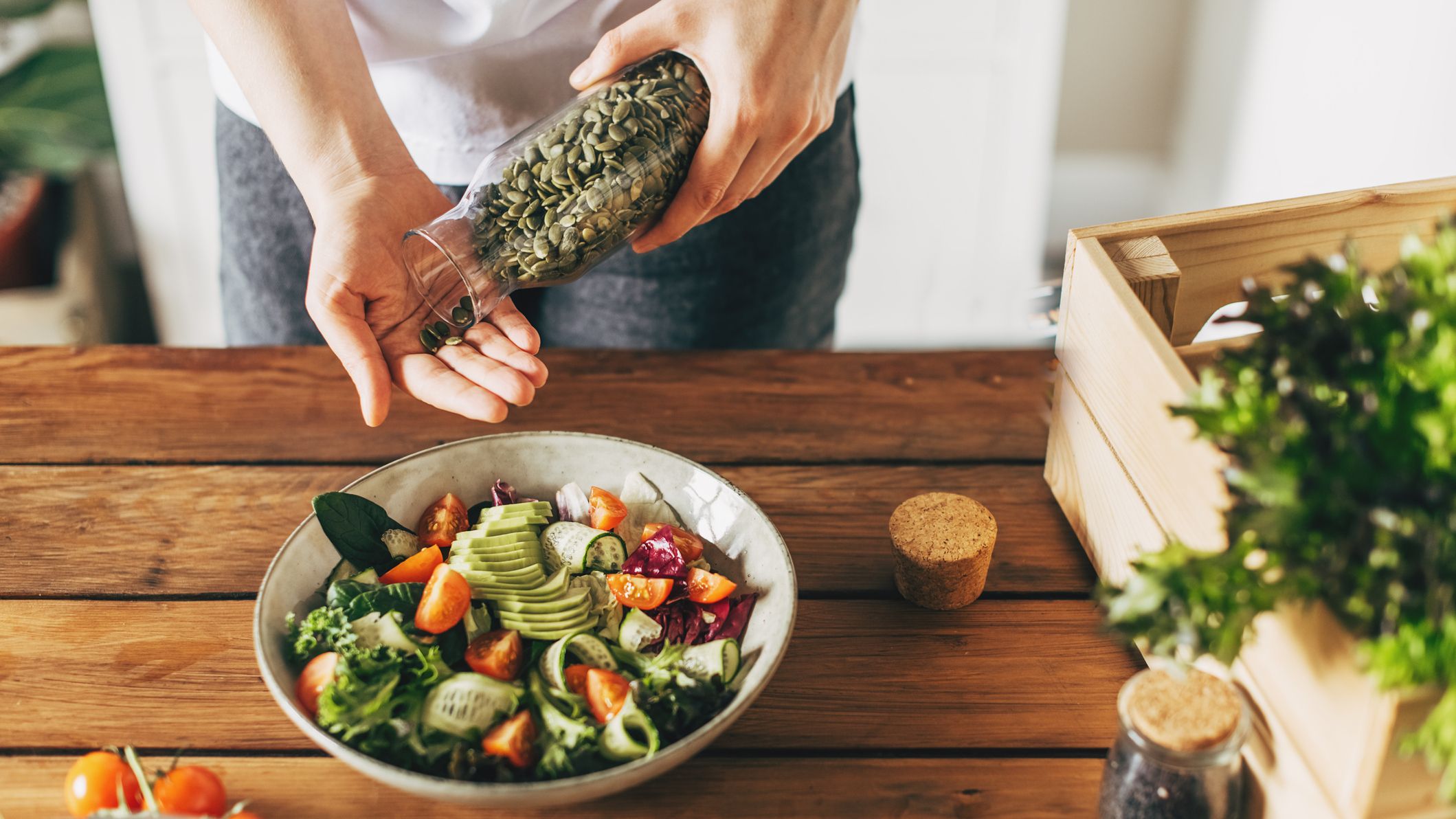Person pours pumpkin seeds into their hand above a bowl of salad