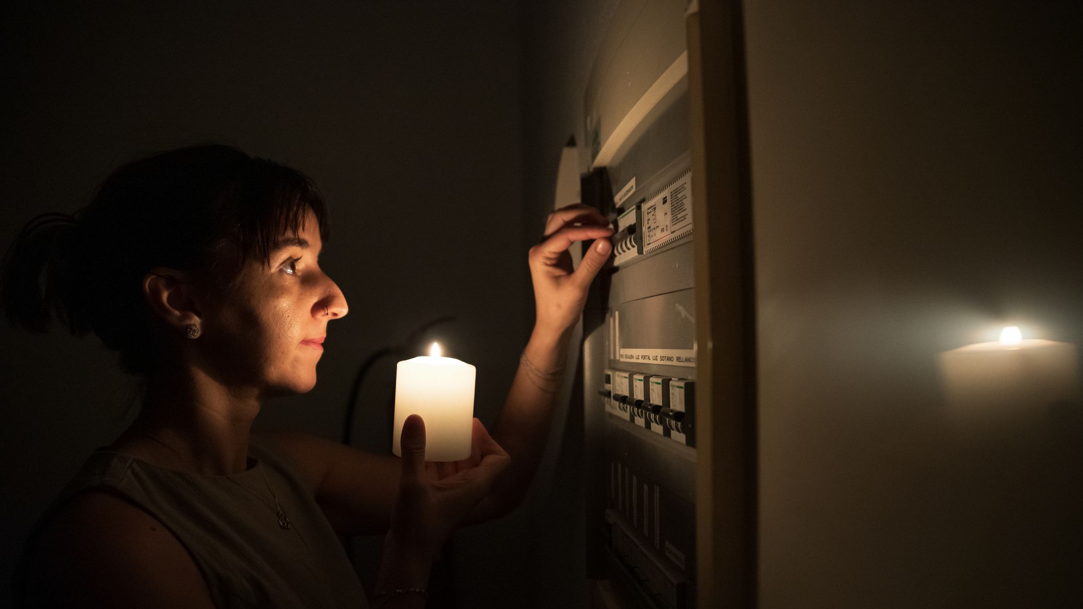a woman holds a candle in one hand while tripping the breaker to try to turn the power on