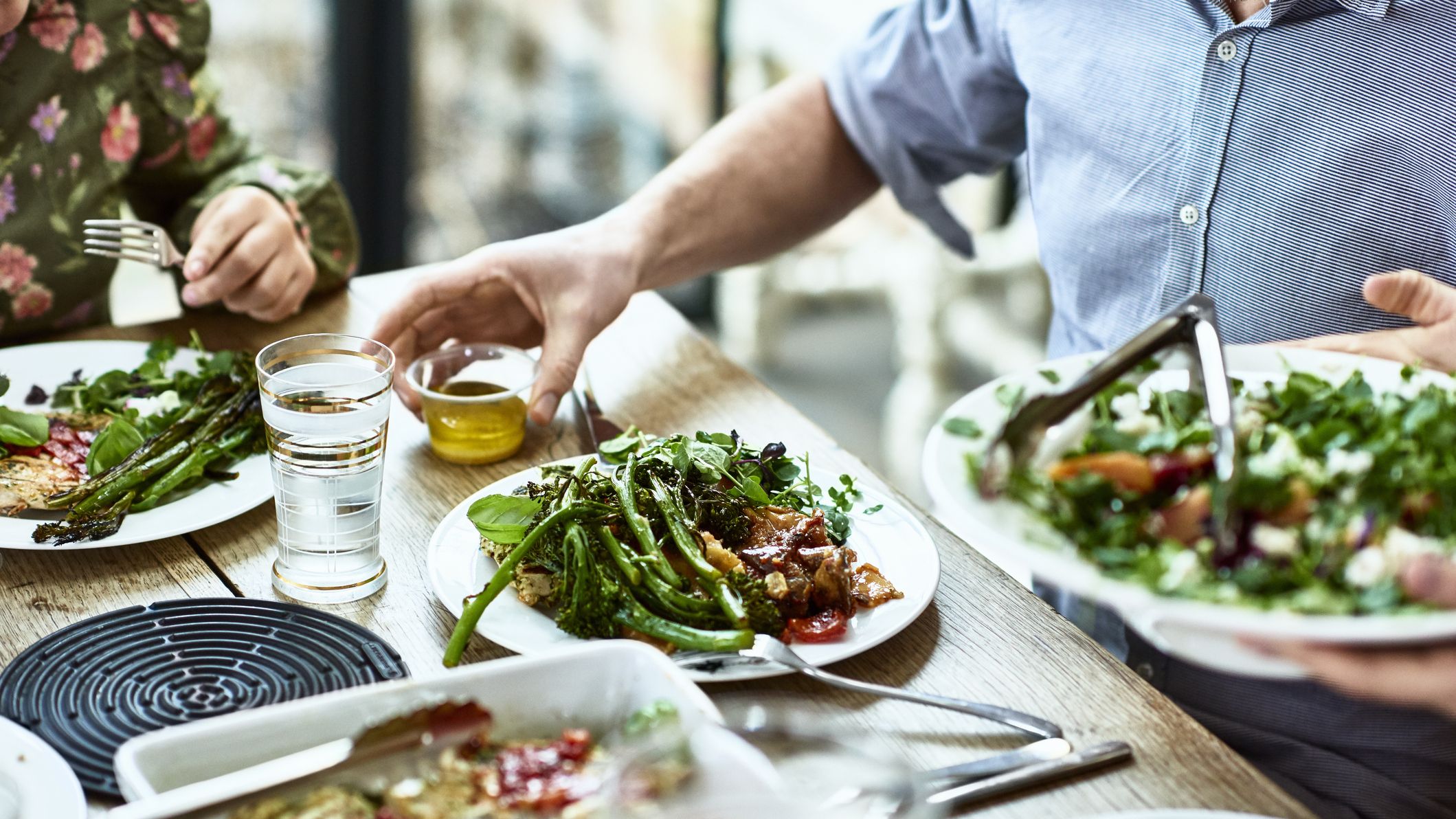 Table with plates and serving dishes of food, with people&#039;s hands and arms seen