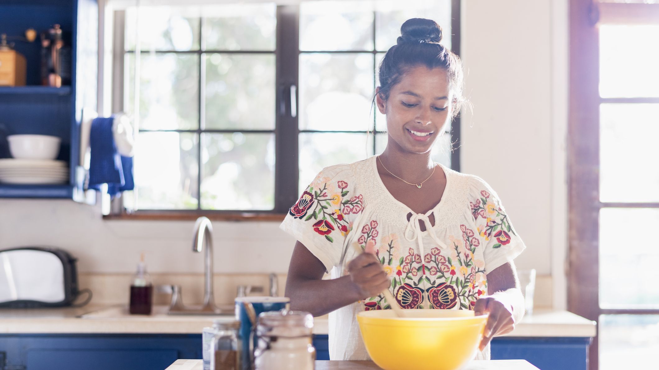 Woman in a kitchen using a wooden spoon to stir something in a yellow mixing bowl