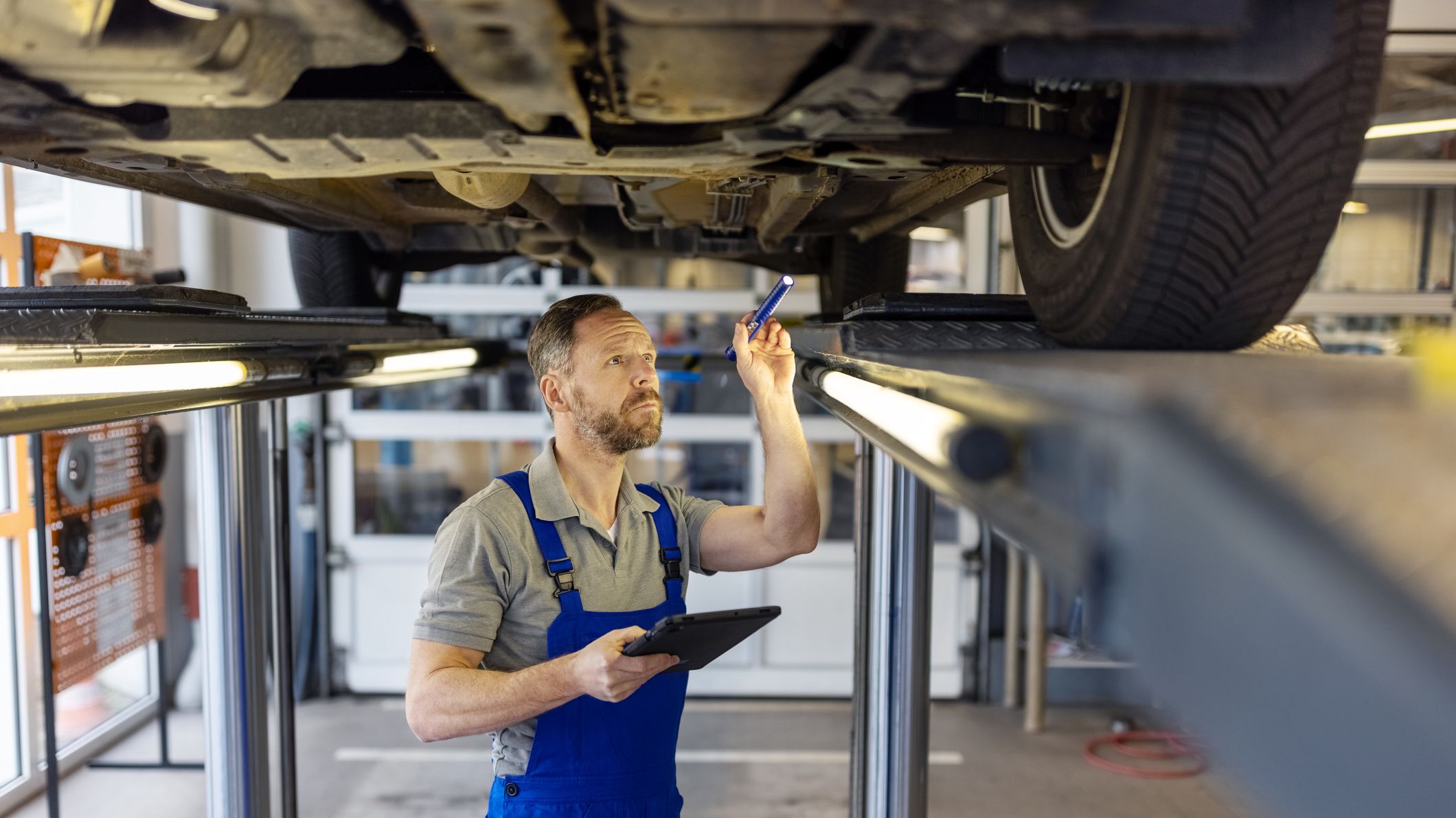 A mechanic inspects the undercarriage of a car at a repair shop.